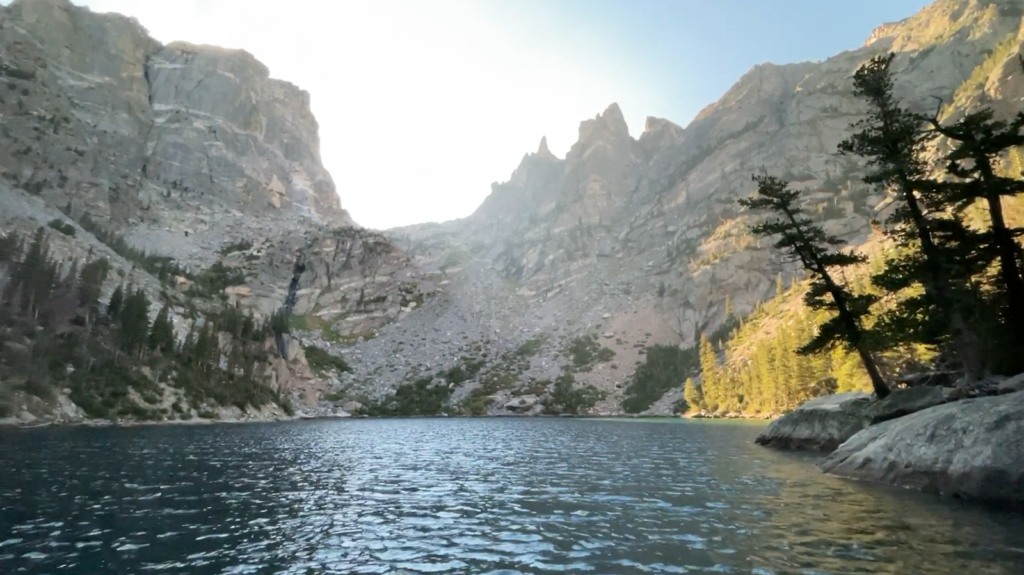 lake near the mountains, trees on the right side on the stones