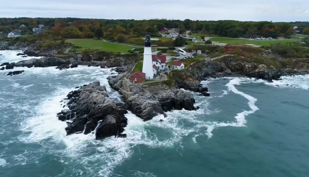 the shore with a lighthouse on it, trees, and town landscape behind