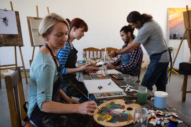 Four people at a table, three are painting individually, while the fourth person stands nearby